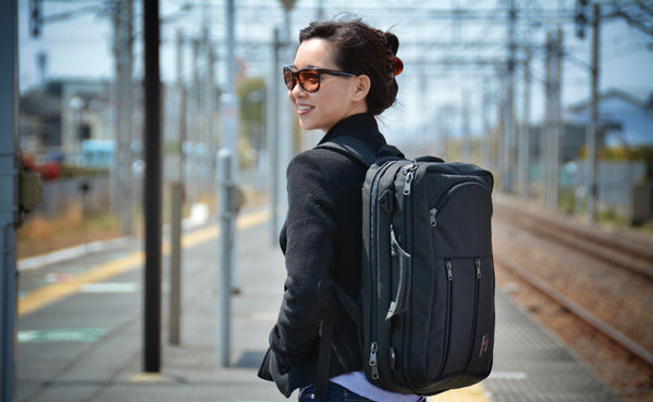 A person carrying a Black 525 Ballistic Western Flyer using the included backpack straps at a light rail station.